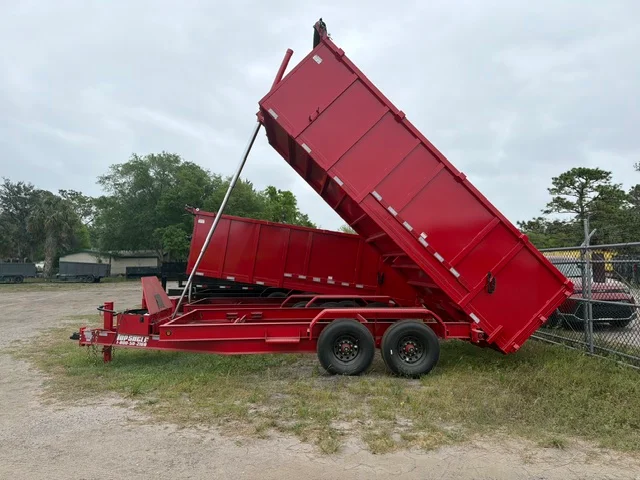 Red dual-axle dump trailer with hydraulic lift raised at full angle, steel construction with side rails