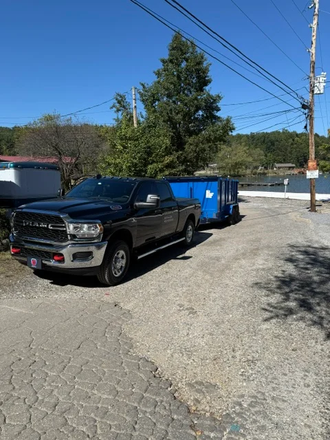 Black pickup truck with blue dumpster trailer loaded for junk removal and hauling