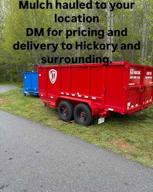 Red dual-axle dump trailer with mulch load on residential driveway