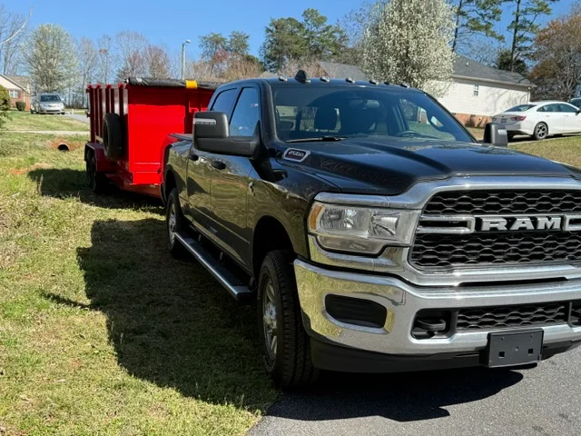 Red dump trailer attached to pickup truck for junk removal and hauling services