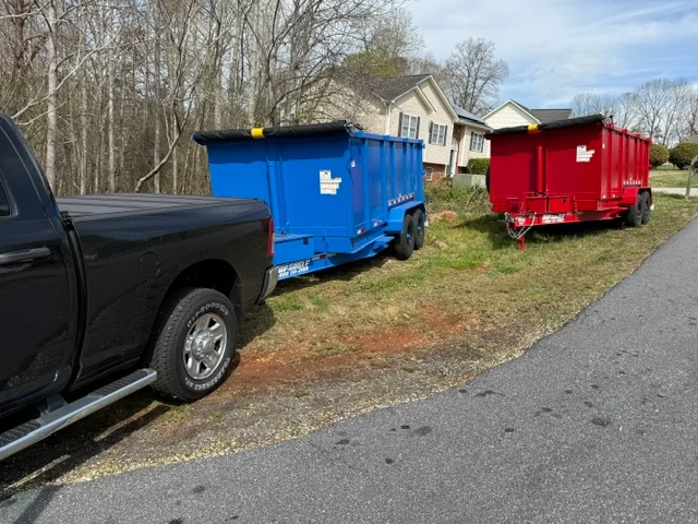 Blue and red commercial dump trailers parked at residential driveway for junk removal