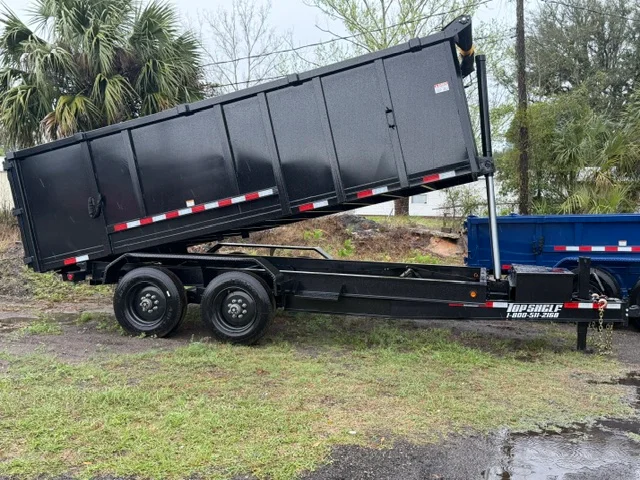 Black steel dump trailer with dual axles and hydraulic lift system on grass