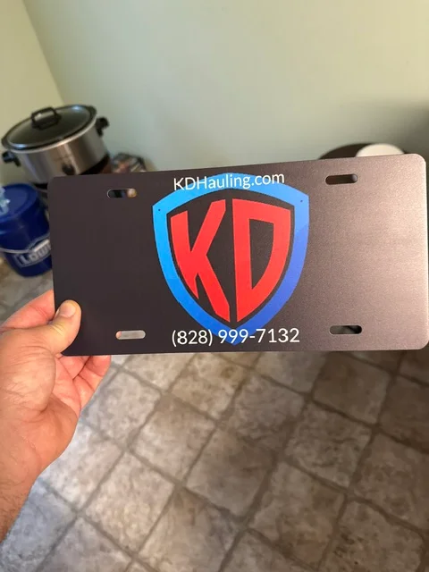 Custom aluminum license plate with red and blue KD shield logo and contact information