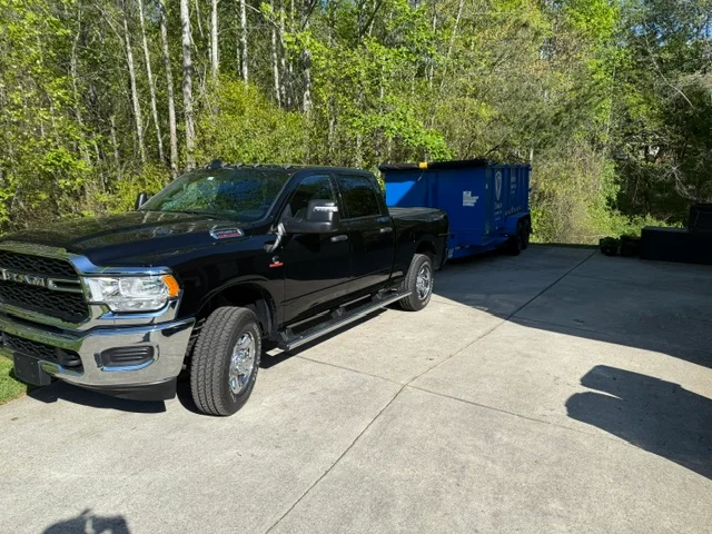 Black pickup truck with blue enclosed trailer parked on concrete driveway