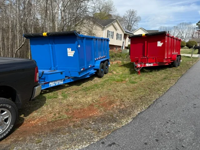Two commercial dump trailers, blue and red, parked at residential driveway for junk removal