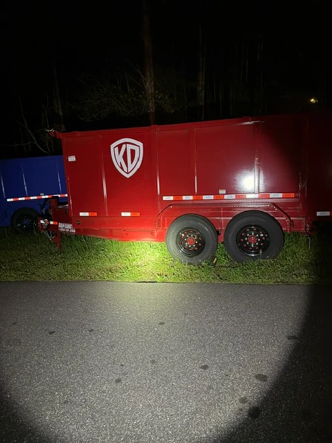 Red vinyl wrap on dual-axle hauling trailer with white logo and reflective safety stripes