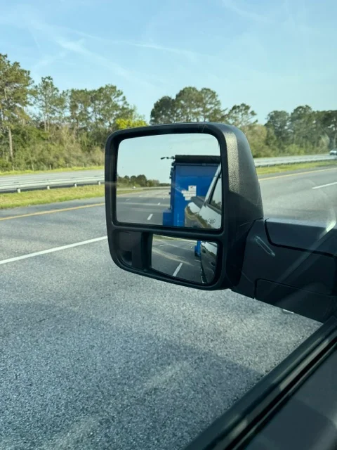 Blue dumpster bin being hauled on flatbed truck bed along highway
