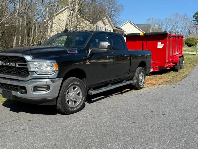 Black Ram pickup truck with red dump trailer in residential driveway
