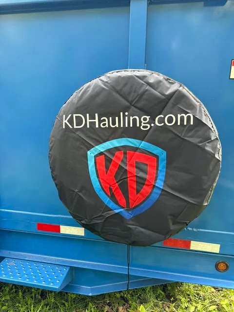 Black vinyl spare tire cover with red and blue shield logo on blue hauling trailer