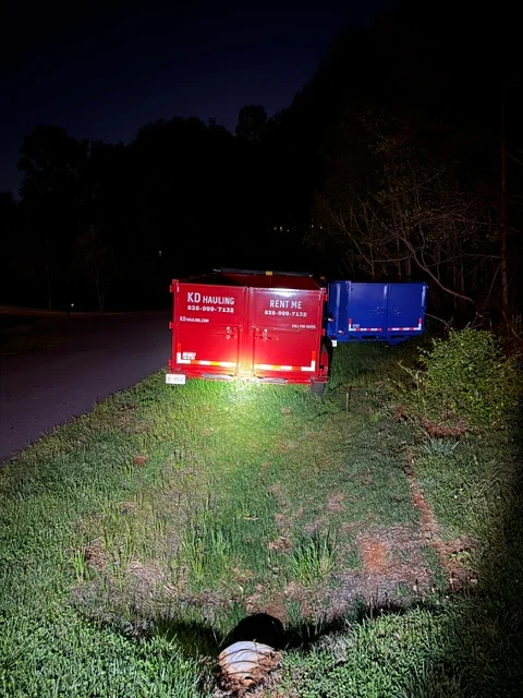 Red and blue dumpster containers on residential property slope at night
