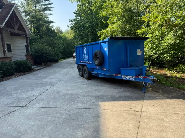 Blue enclosed junk removal trailer parked on residential driveway next to home