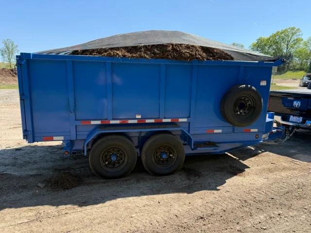 Blue dual-axle dump trailer loaded with mulch and soil material